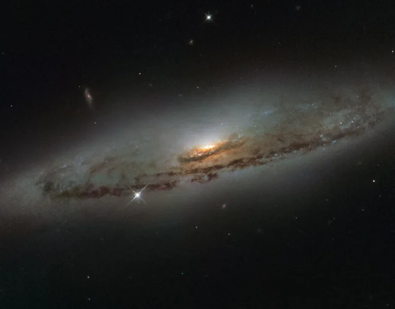 This NASA/ESA Hubble Space Telescope image shows the spiral galaxy NGC 4845, located over 65 million light-years away in the constellation of Virgo (The Virgin). The galaxy’s orientation clearly reveals the galaxy’s striking spiral structure: a flat and dust-mottled disc surrounding a bright galactic bulge. NGC 4845’s glowing centre hosts a gigantic version of a black hole, known as a supermassive black hole. The presence of a black hole in a distant galaxy like NGC 4845 can be inferred from its effect on the galaxy’s innermost stars; these stars experience a strong gravitational pull from the black hole and whizz around the galaxy’s centre much faster than otherwise. From investigating the motion of these central stars, astronomers can estimate the mass of the central black hole — for NGC 4845 this is estimated to be hundreds of thousands times heavier than the Sun. This same technique was also used to discover the supermassive black hole at the centre of our own Milky Way — Sagittarius A* — which hits some four million times the mass of the Sun (potw1340a). The galactic core of NGC 4845 is not just supermassive, but also super-hungry. In 2013 researchers were observing another galaxy when they noticed a violent flare at the centre of NGC 4845. The flare came from the central black hole tearing up and feeding off an object many times more massive than Jupiter. A brown dwarf or a large planet simply strayed too close and was devoured by the hungry core of NGC 4845.