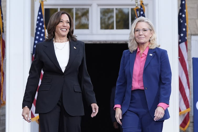 Two women in suits stand on a stage.