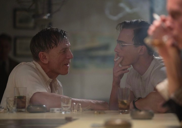 A man sits at a table next to someone smoking a cigarette.